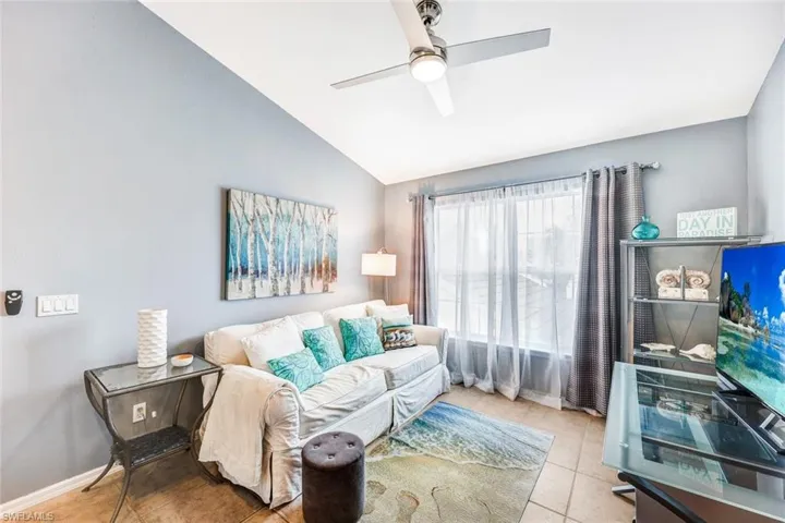 Living room featuring lofted ceiling, ceiling fan, and light tile patterned flooring
