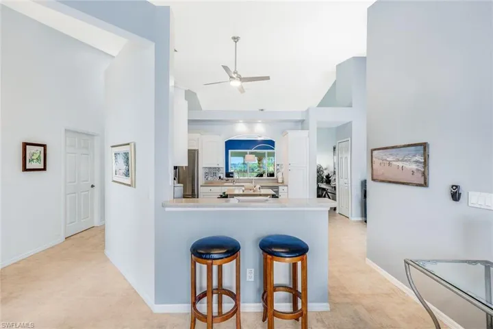 Kitchen with a breakfast bar area, ceiling fan, kitchen peninsula, white cabinetry, and a high ceiling