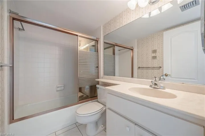 Full bathroom featuring tile patterned flooring, combined bath / shower with glass door, toilet, and vanity