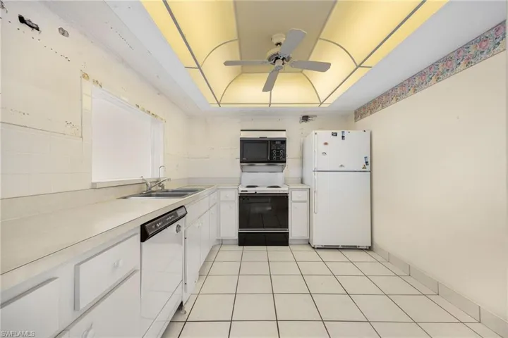 Kitchen featuring white appliances, sink, light tile patterned flooring, white cabinetry, and ceiling fan