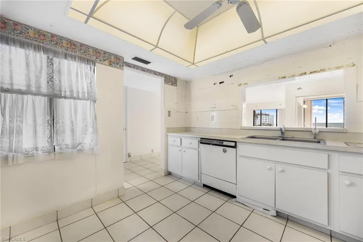 Kitchen with white cabinets, white dishwasher, sink, light tile patterned floors, and ceiling fan