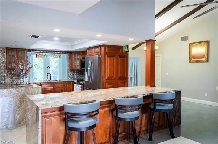Kitchen with brown cabinetry, light stone counters, ornamental molding, ceiling fan, and tasteful backsplash