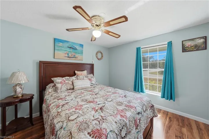 Serene second bedroom with light blue walls, wood-finish laminate flooring, and abundant natural light.