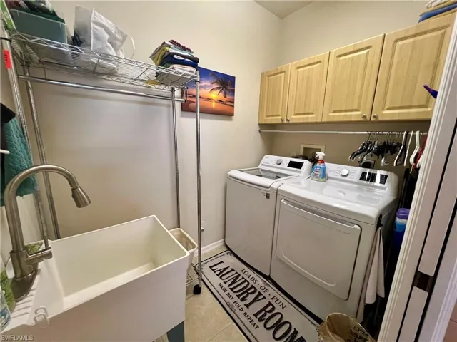 Washroom featuring light tile patterned floors, sink, independent washer and dryer, and cabinets