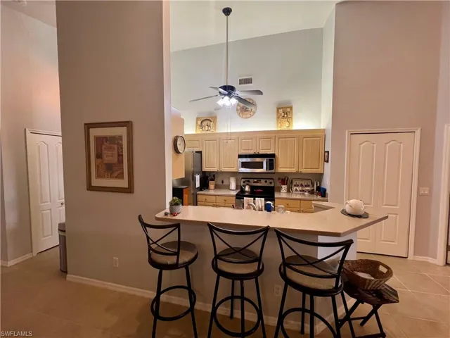 Kitchen featuring a breakfast bar, light tile patterned flooring, high vaulted ceiling, appliances with stainless steel finishes, and ceiling fan