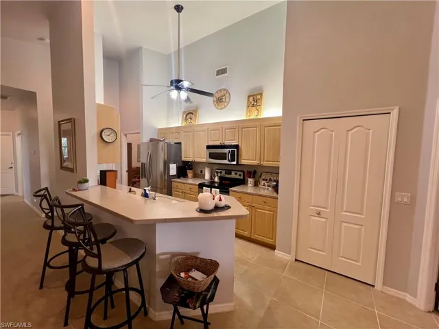 Kitchen with breakfast bar, appliances with stainless steel finishes, light tile patterned floors, a high ceiling, and ceiling fan