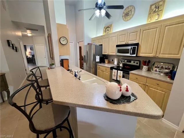 Kitchen featuring sink, a kitchen bar, stainless steel appliances, light tile patterned floors, and a high ceiling