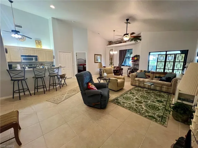 Living room with ceiling fan with notable chandelier, high vaulted ceiling, and light tile patterned flooring