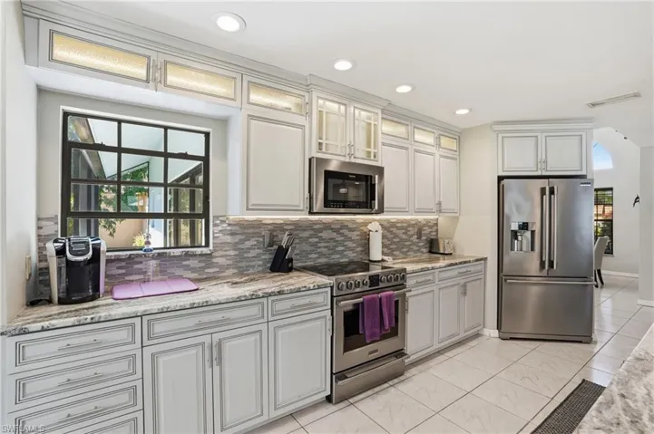 Kitchen with stainless steel appliances, decorative backsplash, glass insert cabinets, light stone countertops, and recessed lighting