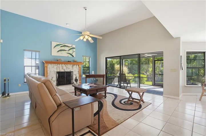 Living area with a towering ceiling, light tile patterned flooring, a stone fireplace, and ceiling fan