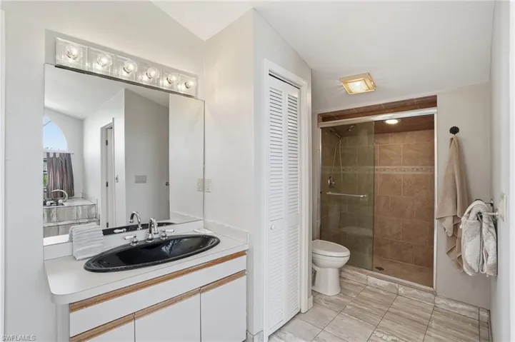 Bathroom featuring a closet, vanity, a shower stall, and light tile patterned flooring