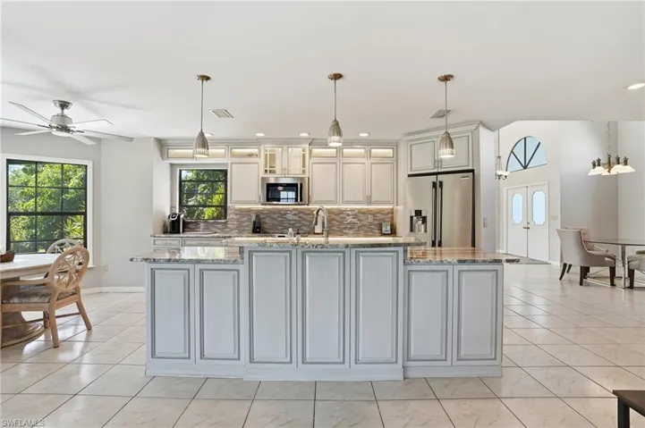 Kitchen with light stone countertops, decorative light fixtures, stainless steel appliances, a center island with sink, and glass insert cabinets