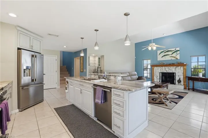 Kitchen with appliances with stainless steel finishes, white cabinetry, light stone counters, open floor plan, and pendant lighting
