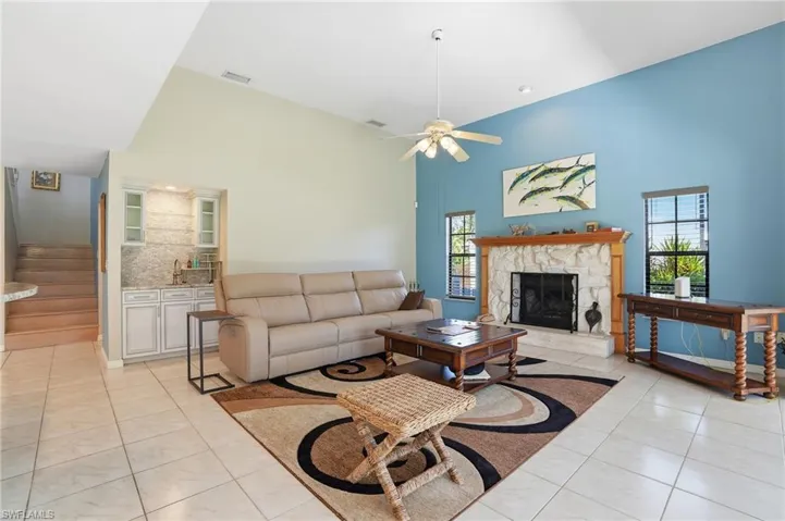 Living room with stairs, a high ceiling, a ceiling fan, a stone fireplace, and light tile patterned floors
