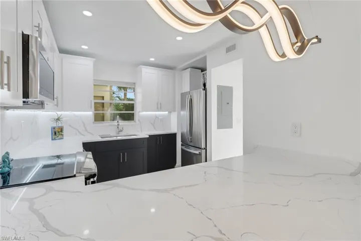 Kitchen featuring visible vents, stainless steel appliances, a sink, dark cabinetry, and light stone counters