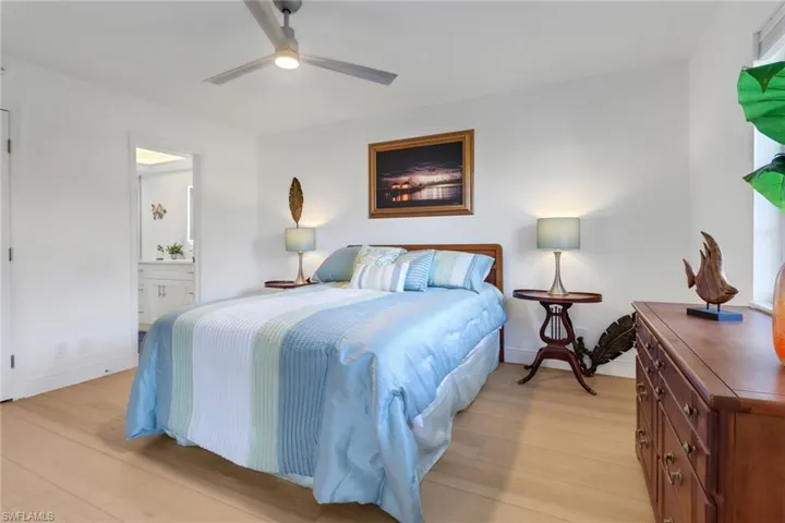 Bedroom featuring a ceiling fan, ensuite bathroom, baseboards, and light wood-style floors