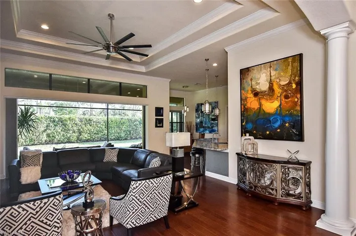 Living area featuring ornate columns, a tray ceiling, dark wood finished floors, ornamental molding, and recessed lighting