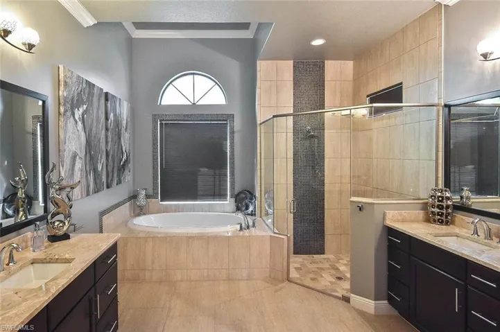 Bathroom with two vanities, a stall shower, a bath, ornamental molding, and light tile patterned floors