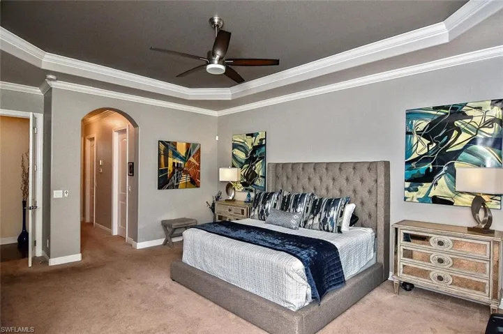 Carpeted bedroom with arched walkways, ornamental molding, a tray ceiling, and a ceiling fan
