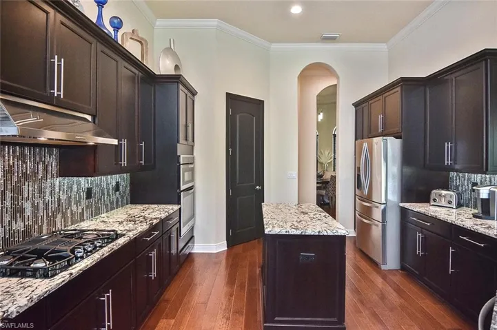 Kitchen featuring backsplash, arched walkways, ornamental molding, a kitchen island, and light stone counters