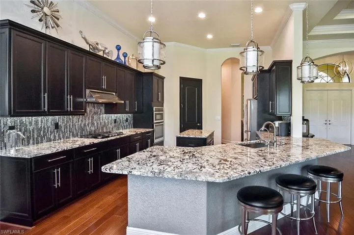 Kitchen featuring light stone countertops, pendant lighting, crown molding, a kitchen island, and decorative backsplash