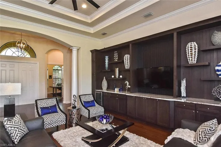 Living area with arched walkways, dark wood-style floors, crown molding, a raised ceiling, and decorative columns