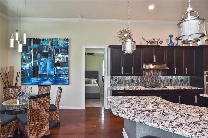 Kitchen featuring light stone countertops, hanging light fixtures, ornamental molding, dark wood-style flooring, and decorative backsplash