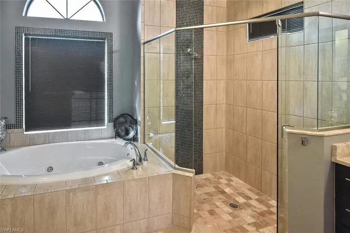 Bathroom with a tub with jets, a stall shower, and vanity