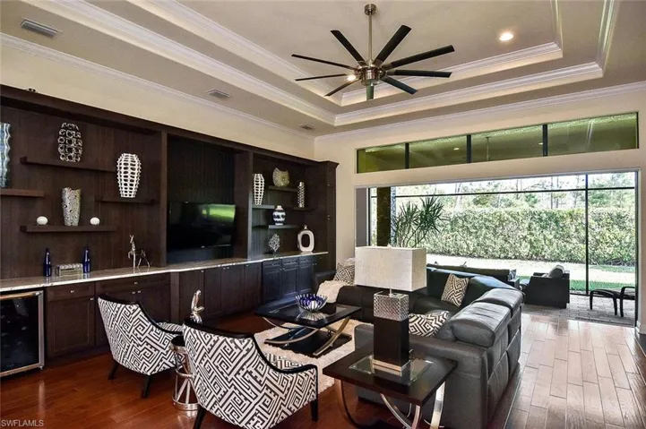 Living room featuring a raised ceiling, beverage cooler, dark wood-style floors, crown molding, and a ceiling fan