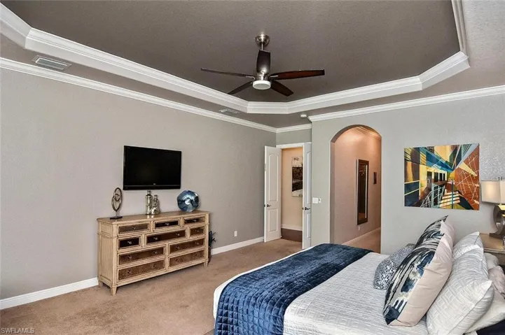 Carpeted bedroom with a raised ceiling, arched walkways, crown molding, and a ceiling fan