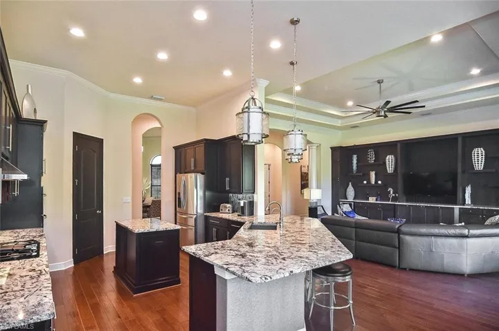 Kitchen featuring crown molding, decorative light fixtures, a kitchen island, arched walkways, and light stone countertops