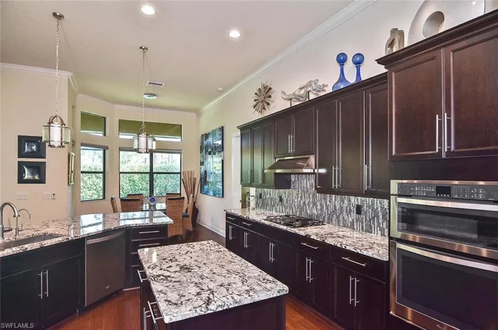 Kitchen featuring stainless steel appliances, hanging light fixtures, crown molding, light stone countertops, and dark wood-style flooring
