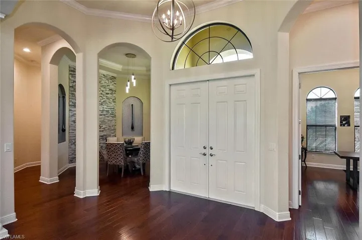 Foyer entrance featuring arched walkways, dark wood-style floors, ornamental molding, a chandelier, and a high ceiling