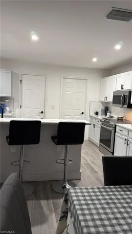 White cabinetry, stainless steel appliances, wood-finish flooring, recessed lighting, and a kitchen island with seating