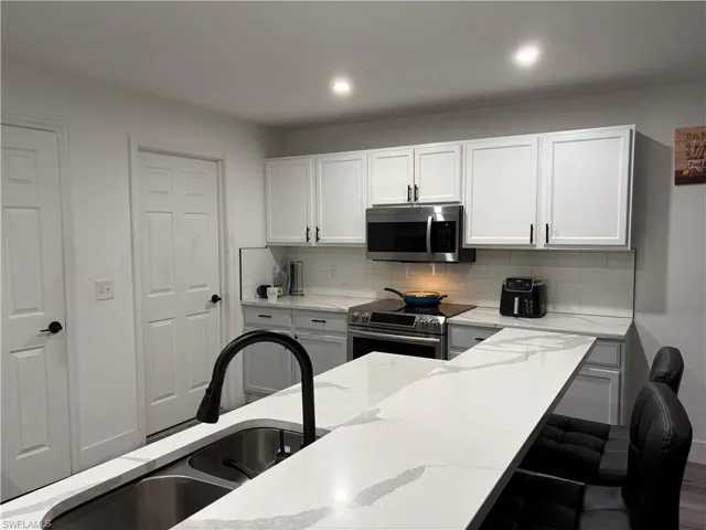 White shaker-style cabinetry, stainless steel appliances, light-toned countertops, subway tile backsplash, and a large kitchen island with an undermount sink