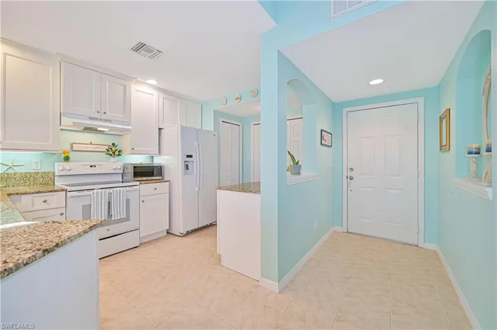 Kitchen with white appliances, light stone countertops, white cabinetry, and light tile floors