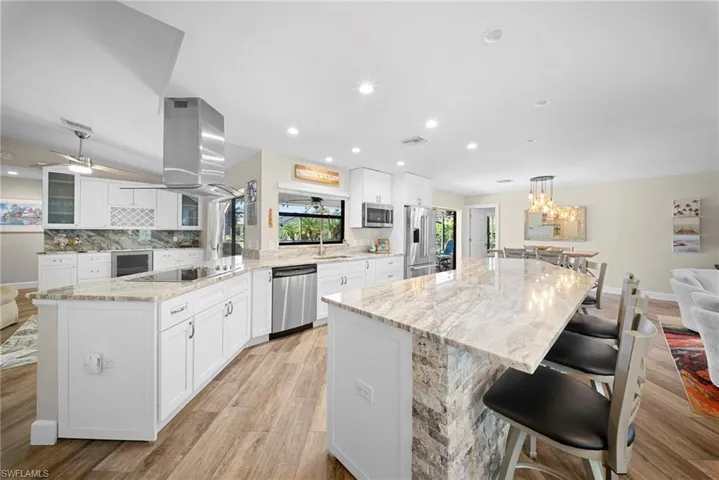 Spacious kitchen featuring an expansive island with stone veneer detailing, white shaker-style cabinetry, stainless steel appliances, and wood-finish flooring