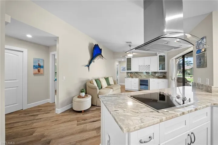Kitchen island featuring a built-in cooktop, light-toned stone countertops, and white cabinetry with chrome hardware