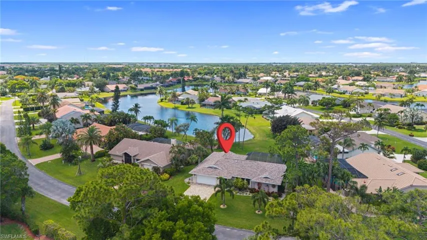 Lakeside property featuring a spacious lot, mature palm trees, an attached garage, and a tiled roof, set within a residential community with water access
