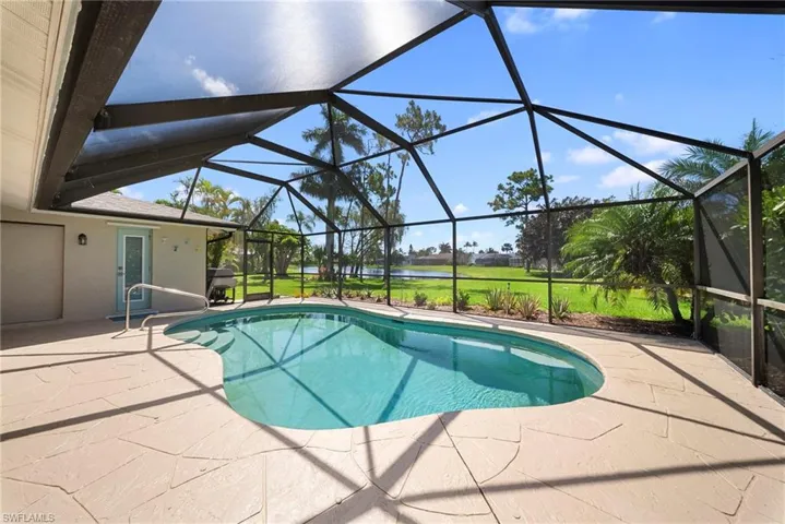 Screened enclosure with a freeform swimming pool, spacious paver patio, and lush green landscaping