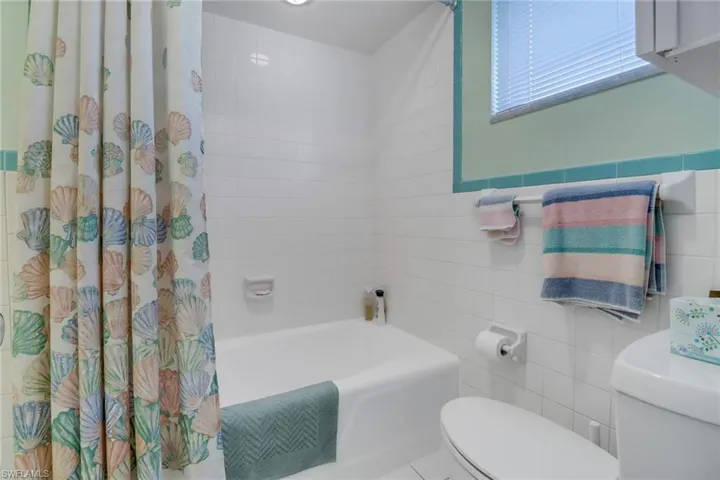 Bathroom with shower / bathtub combination with curtain, tile walls, and toilet