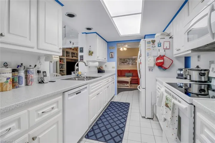Kitchen with ceiling fan, white cabinets, light tile patterned floors, white appliances, and sink