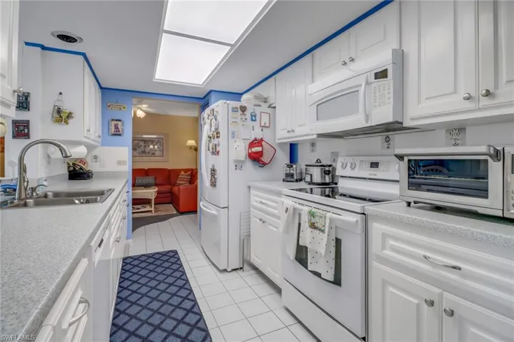 Kitchen featuring ceiling fan, white cabinetry, light tile patterned floors, white appliances, and sink