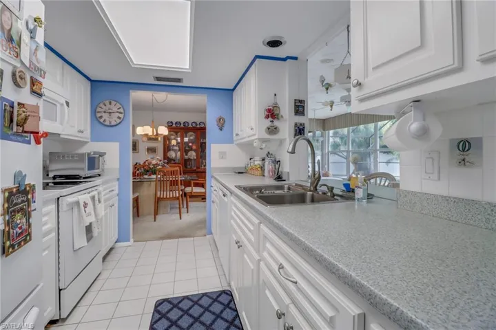 Kitchen featuring white cabinetry, hanging light fixtures, light carpet, white appliances, and sink