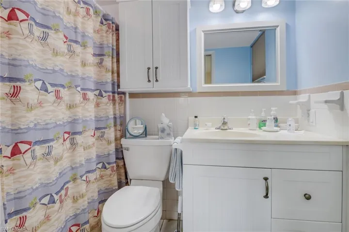 Bathroom featuring tasteful backsplash, tile walls, vanity, and toilet