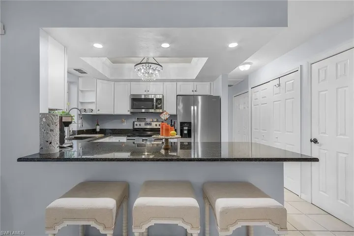 Kitchen with a kitchen breakfast bar, kitchen peninsula, a tray ceiling, white cabinetry, and appliances with stainless steel finishes