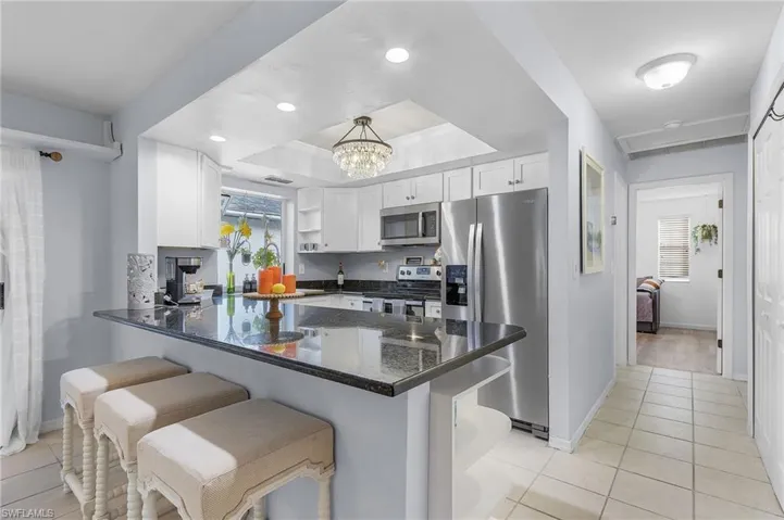 Kitchen featuring kitchen peninsula, a raised ceiling, appliances with stainless steel finishes, a breakfast bar, and white cabinetry