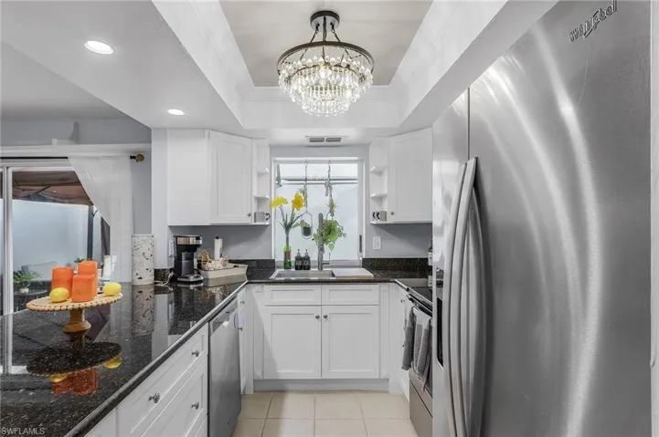 Kitchen with stainless steel appliances, granite counters, a tray ceiling, sink, decorative light fixtures, and white cabinetry