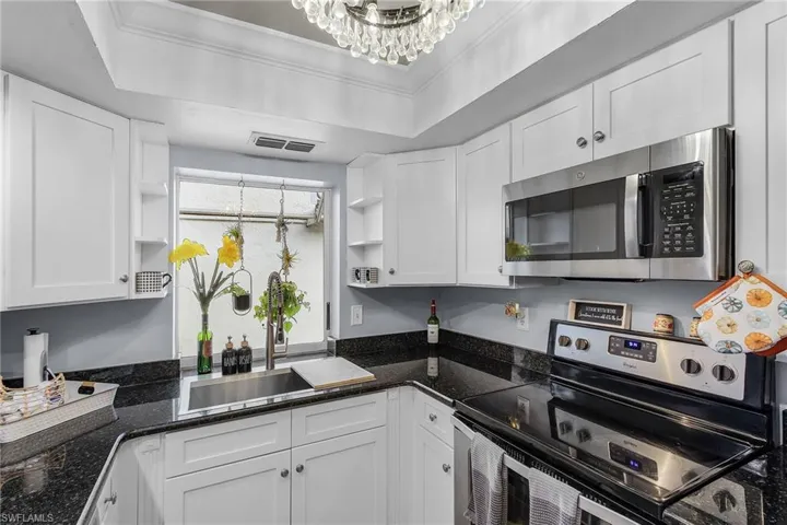 Kitchen with appliances with stainless steel finishes, a tray ceiling, white cabinets, and dark stone counters