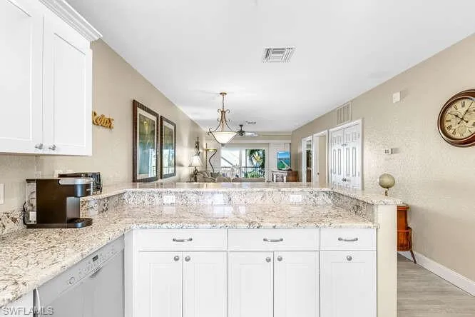 Kitchen featuring white cabinetry, a peninsula, dishwasher, and light stone countertops